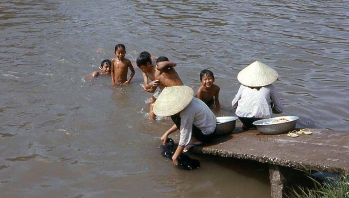 Bien Thuy Air Base. Village hamlet along river. Lazy Sunday, Mamasans do laundy, and kids play in river. MSgt Summerfield, 1968: 07