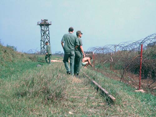 1. Đông Hà Air Field: Mines and Trip flares placed on perimeter. Look close and notice the inplace railroad rail between the men walking and the man squatting (near their feet) placing a flare.
