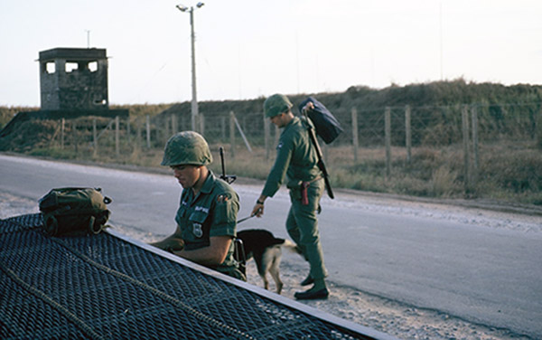 19. Đà Nẵng AB, K-9 Growl Pad: Gary Eberbach (right) walks Bucky to post. 1965.