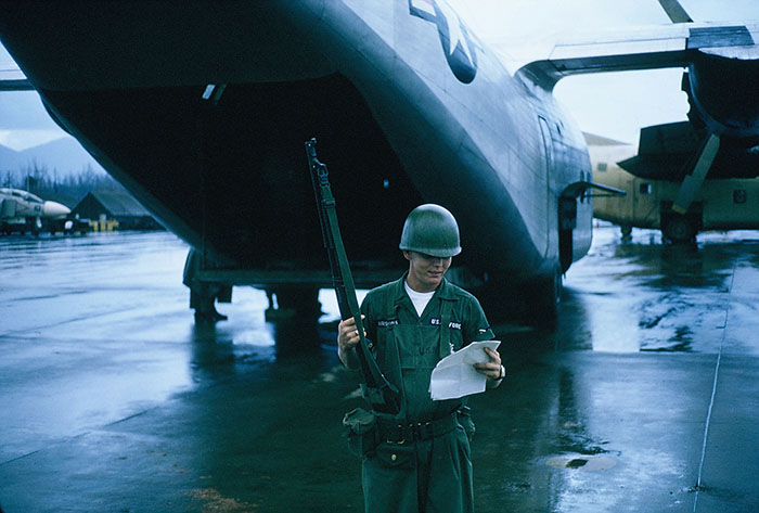 6. Đà Nẵng AB, flight line: A2C Parsons, reading Post SOPs for C-123 flight line, between raindrops. 1965.