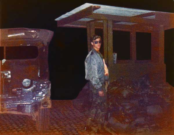 3. NKP flight line Entrance Gate, April 1975: Sgt Bacon is in front of the gate standing next to my jeep. I didn't send it earlier because I took it at night and it's very dark. Photo by: Jonathan Faulkner, 56th SPS, NKP.