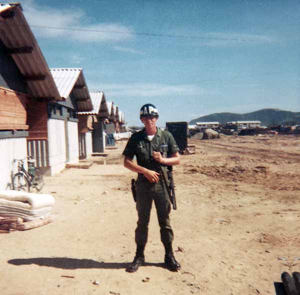 Photo #11 (Nha Trang): This is me getting ready to go on duty. I must have been assigned to the Main Gate as I don't recall helmets being worn on any other post. This was taken behind the hooches prior to the move to the concrete barracks. At the time of this photo we maintained our weapons in the hooches.