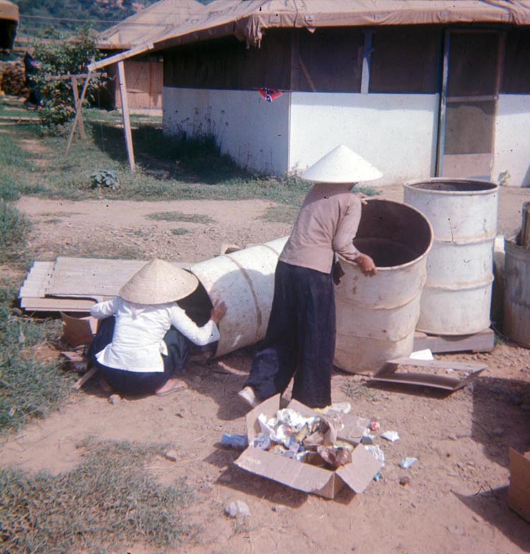 23. Phan Rang Air Base: 1966: Tent-Hut with mamasans digging through trash for C-Rats. Note the CSA Rebel Flag on the hut's corner.